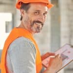 Bearded man in a helmet holding blueprints