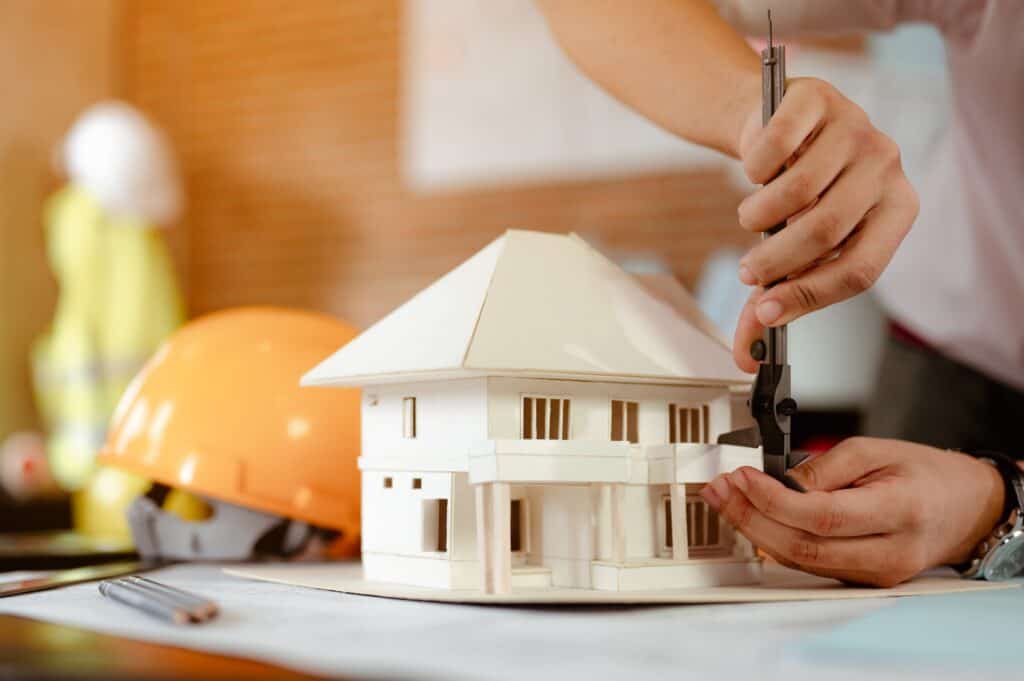 Close up of male architect hands measuring and making model house on the desk at sunset.