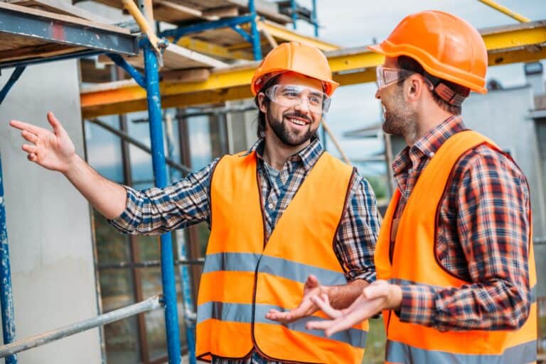 happy builders in reflective vest and hard hat pointing at building house